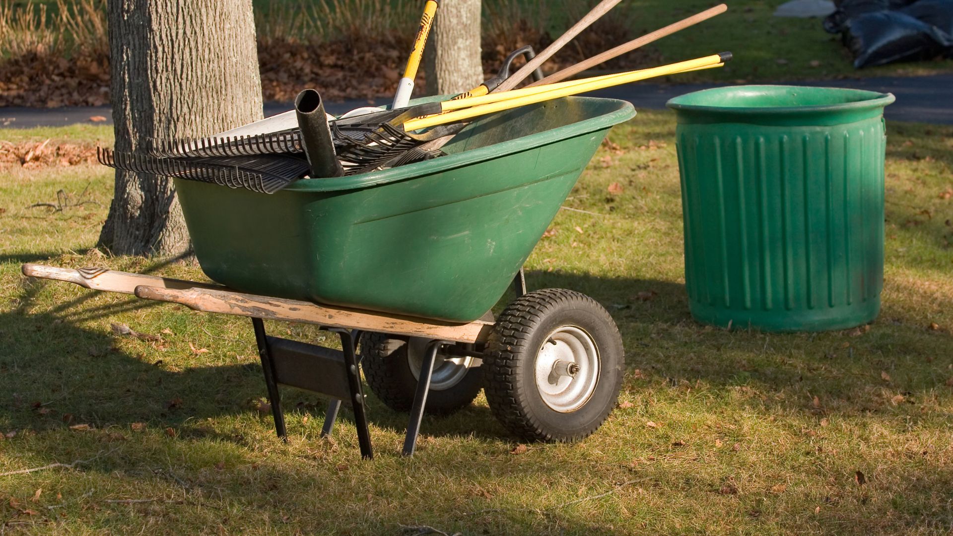 A green wheelbarrow with a green trash can next to it